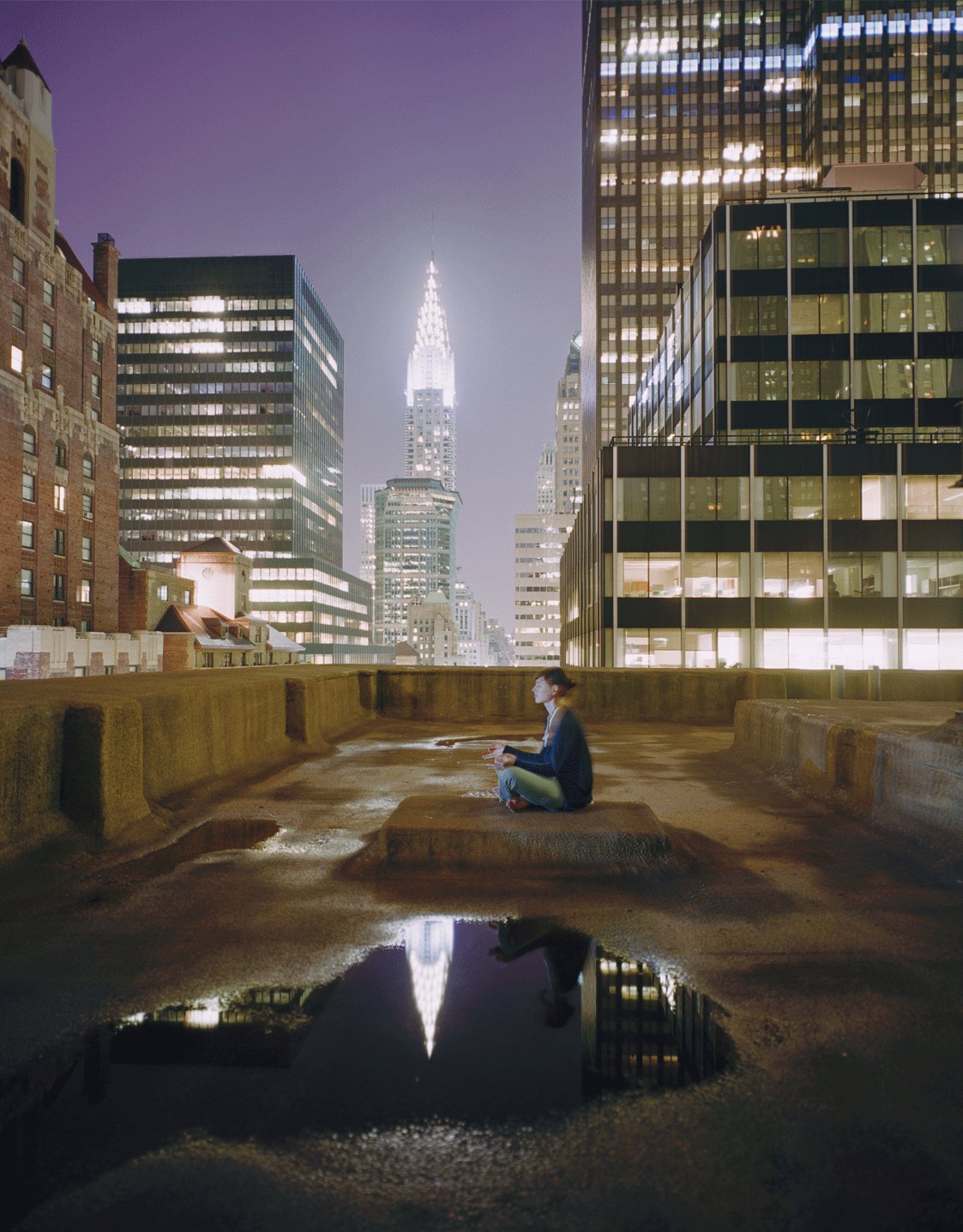 Photographie d’art d’André Wagner: Sur un toit, une personne est assise entre de grands immeubles éclairés — Coming down, Usa.