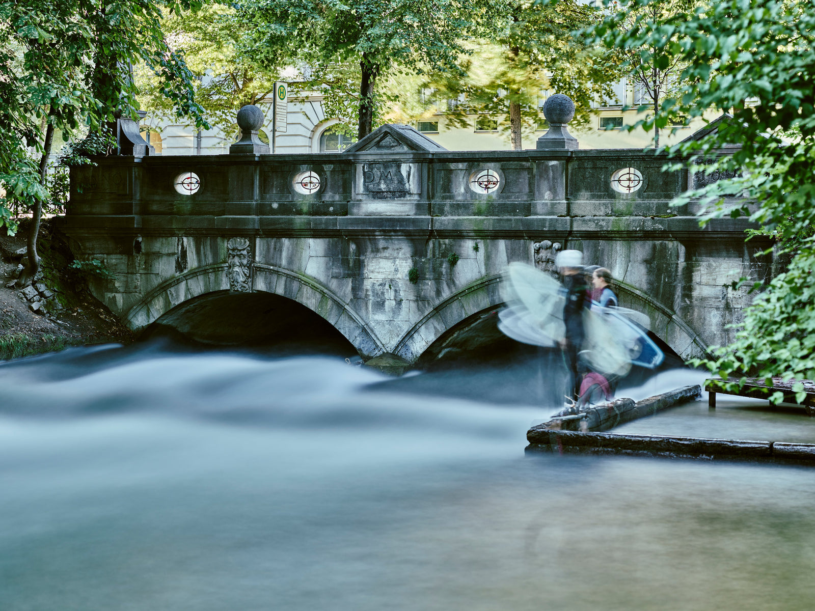 Photographie d’art d’André Wagner: Sous un pont de pierre à deux arches, l’eau avance comme une surface douce et bleu clair — Eisbach Surfer 2, Deutschland.