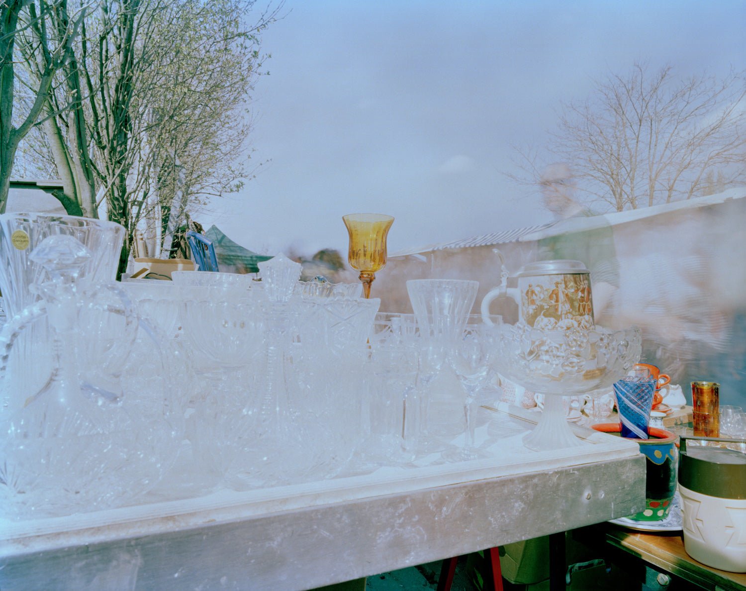 Fine art photography by André Wagner: Pale glasses and vessels crowd a horizontal stall — Flea Market, Deutschland.