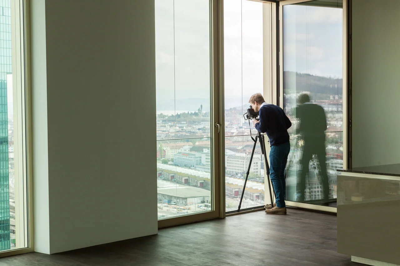 Photographer with a tripod at a large window overlooking a city