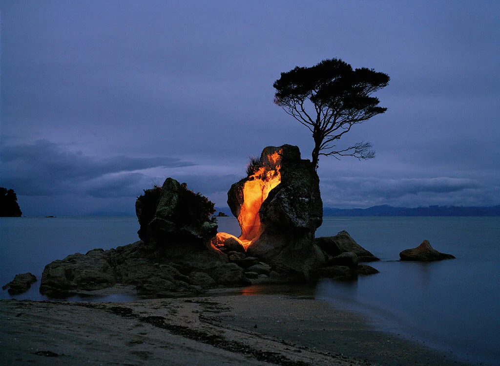 Fine art photograph of an illuminated rock and tree beside water at dusk