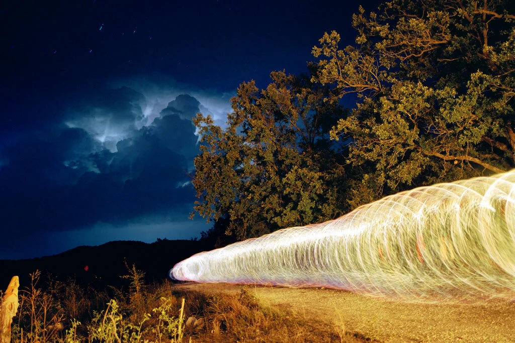 Fine art photograph of a bright light trail and a tree beneath a night sky