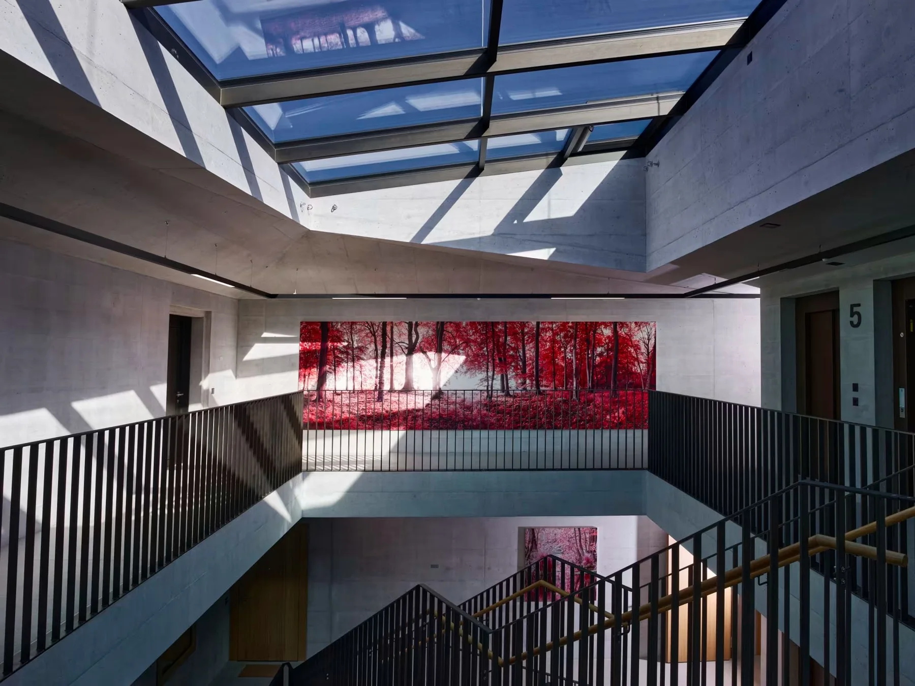 Fotokunst mit rotem Waldmotiv in einem Treppenhaus unter einem Glasdach