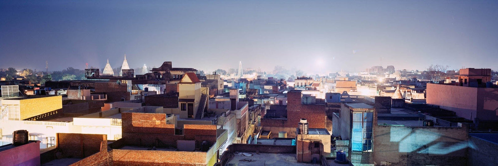 Fine art photography by André Wagner: Flat roofs, walls and small structures extend across a broad panorama — Fullmoon in vrindavan, Indien.