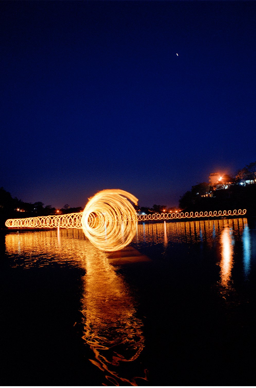 Photographie d’art d’André Wagner: Un cercle de lumière dorée se détache devant une étendue d’eau sombre — Ganga runner, Indien.