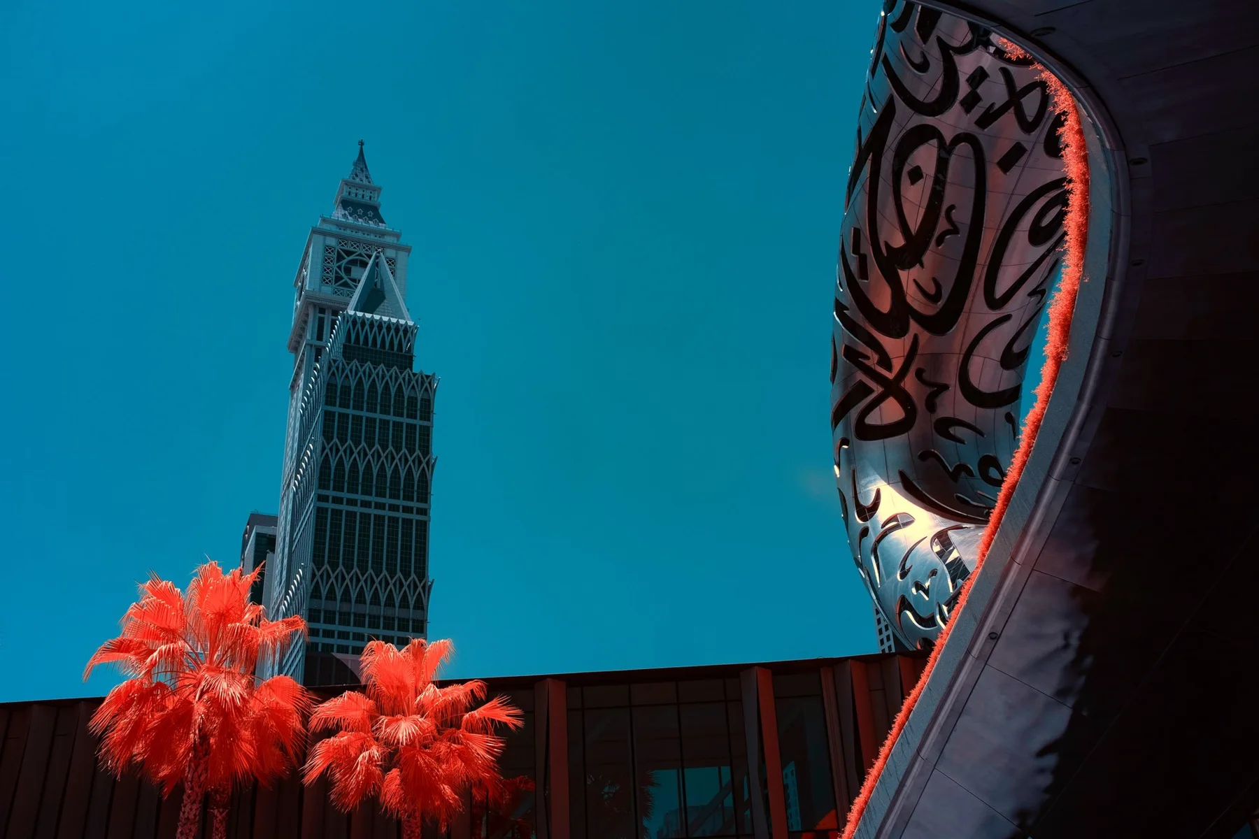 Fa&ccedil;ade courbe d&rsquo;un mus&eacute;e &agrave; c&ocirc;t&eacute; d&rsquo;une haute tour et de palmiers rouges.