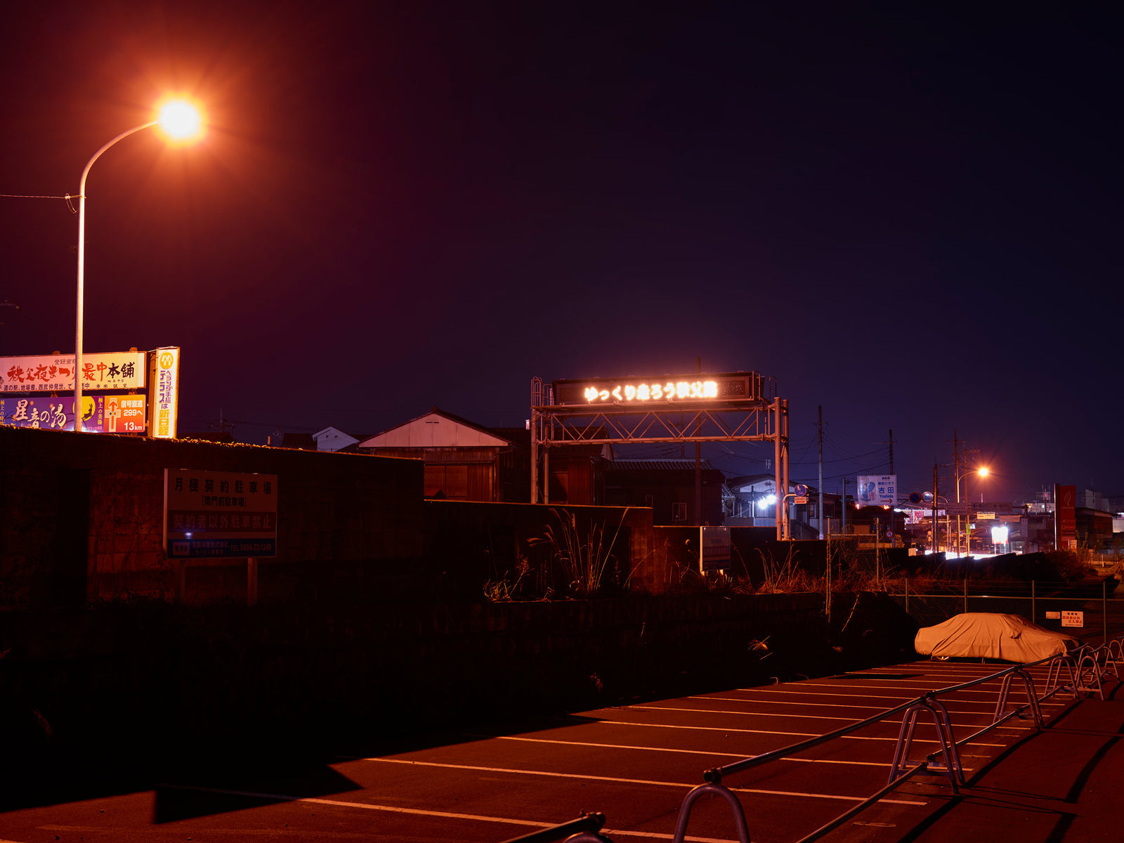 Fotokunst von André Wagner: Eine einzelne gebogene Straßenlampe leuchtet orange über einem dunklen Straßenraum — Japan Street.
