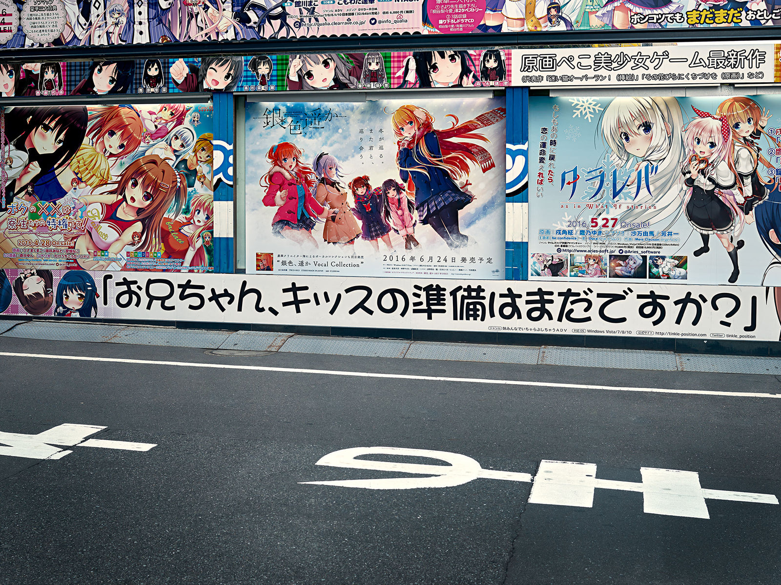 Fine art photography by André Wagner: A wall covered with manga figures and lettering rises above a dark band of asphalt — Manga street, Japan.