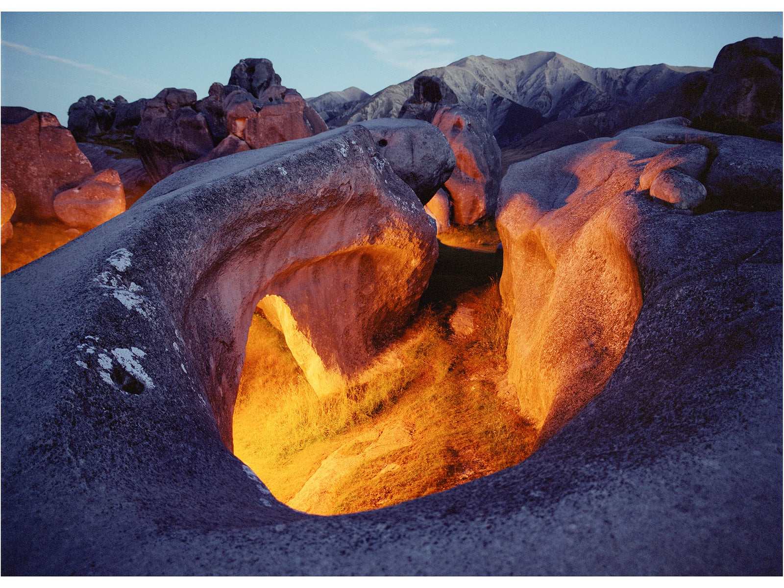 Fine art photography by André Wagner: Large rounded rocks enclose a deep opening filled with warm orange light — Maori spirit, Neuseeland.