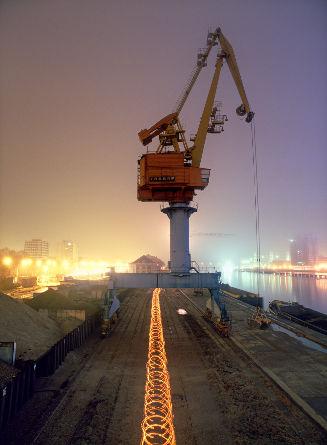Photographie d’art d’André Wagner: Une grande grue se dresse à l’extrémité d’une surface sombre et rectiligne — Media Spree Crane, Deutschland.