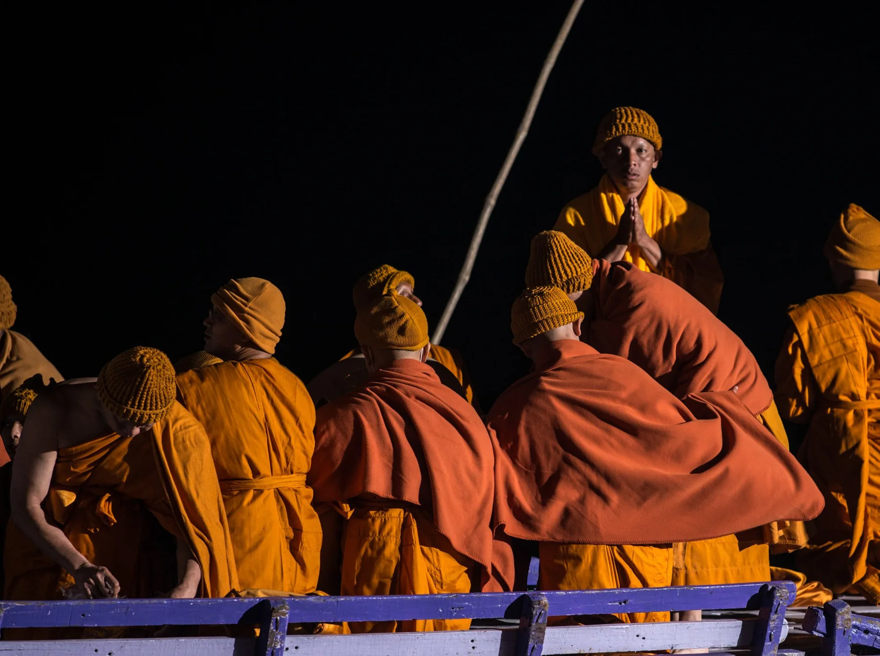 Menschen in orangefarbenen T&uuml;chern sitzen auf einem Boot bei Nacht.