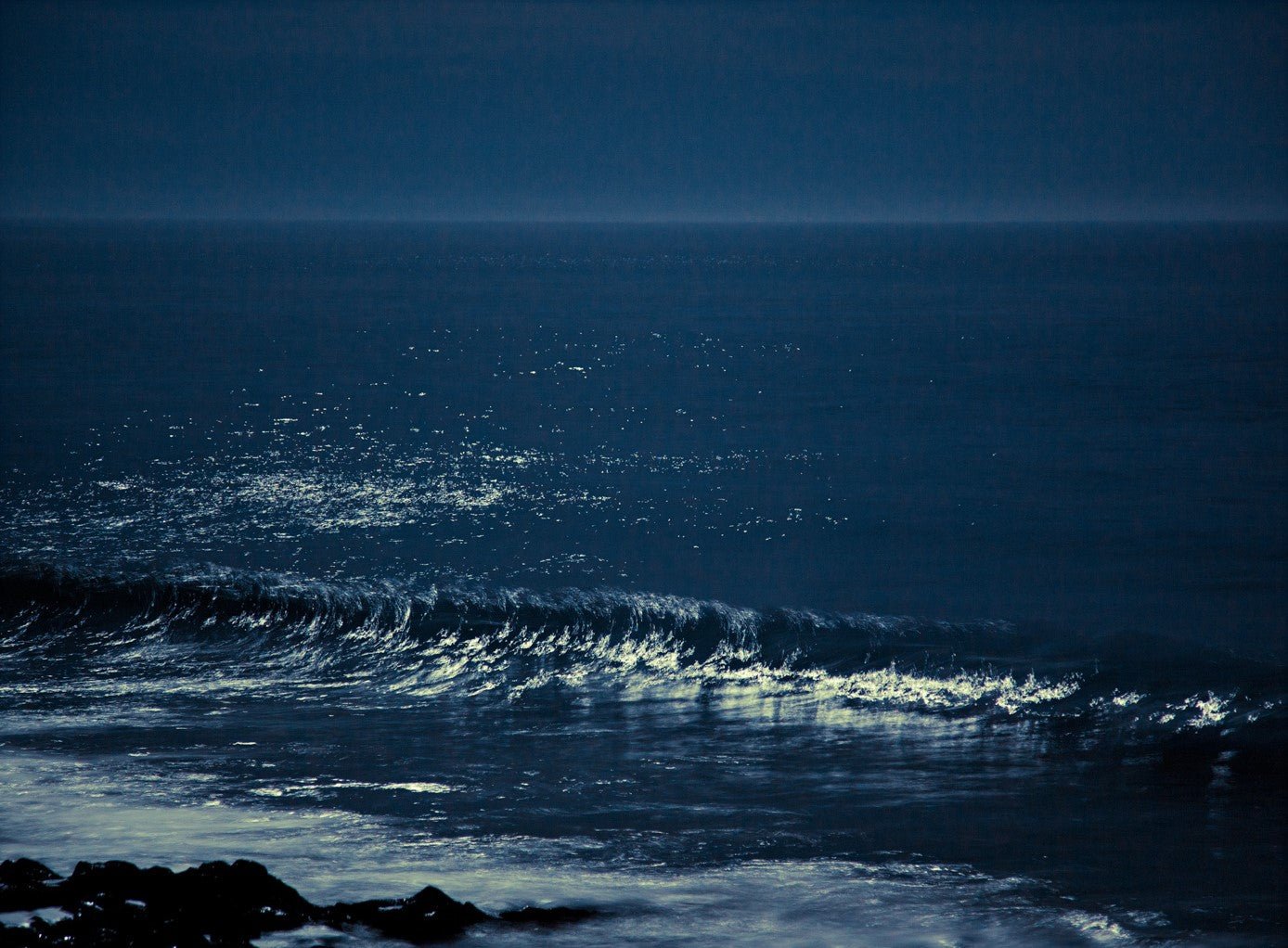 Photographie d’art d’André Wagner: Plusieurs vagues basses s’approchent d’une rive sombre et pierreuse — Moonwaves II, Portugal.