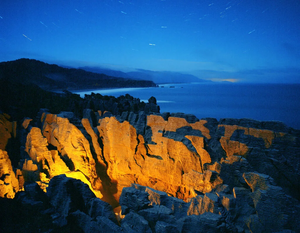 Night landscape photograph of orange-lit rocks beneath a blue sky