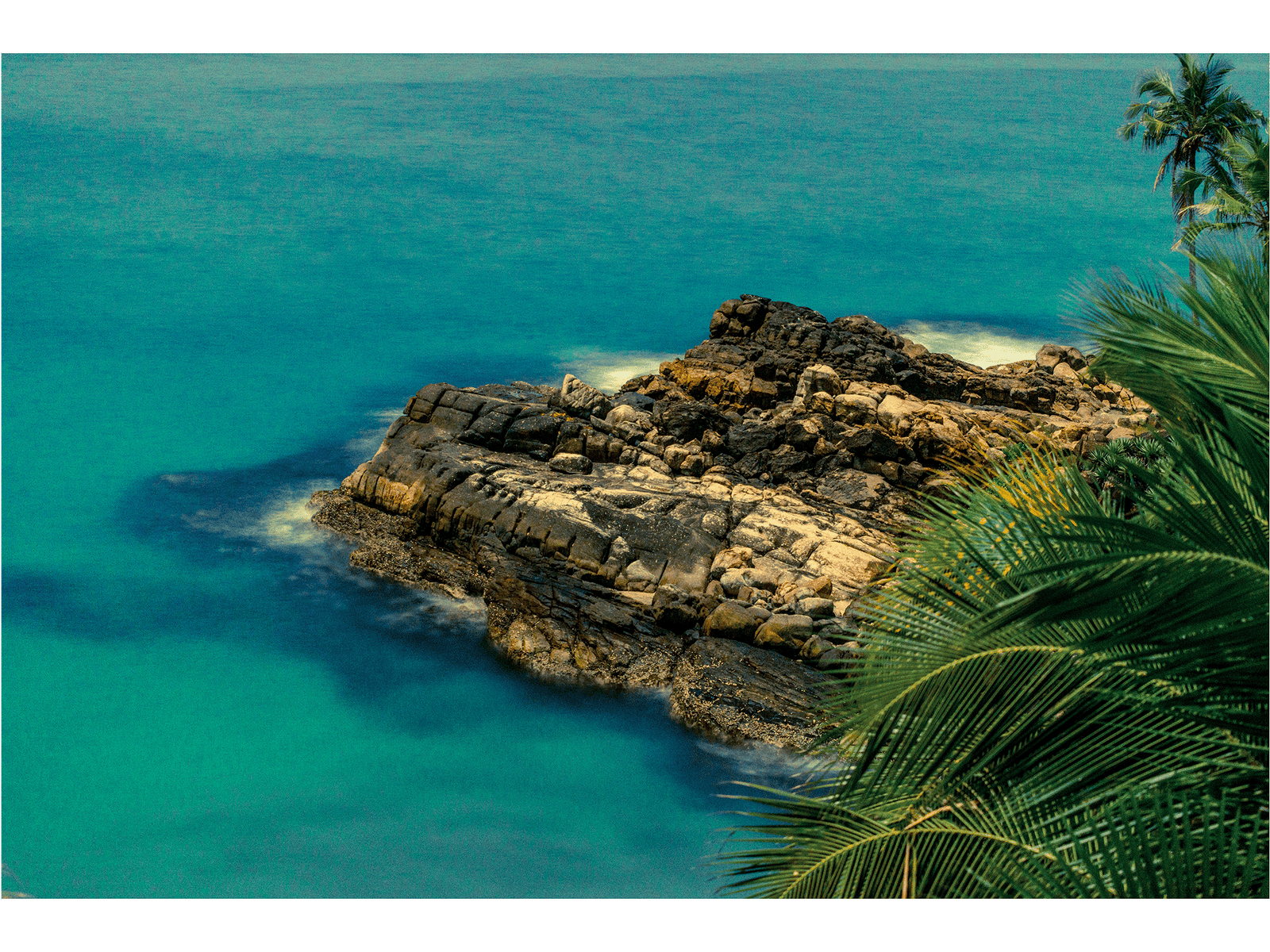Fine art photography by André Wagner: A fractured rocky projection extends from the right into turquoise water — Ocean rock in kerala, Indien.