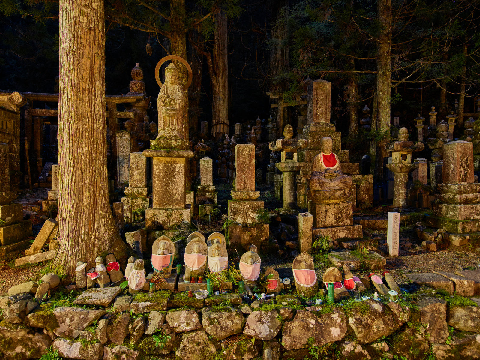 Photographie d’art d’André Wagner: De nombreuses figures de pierre et formes dressées se tiennent sur un socle bas et irrégulier entre les arbres — Oku-No-In Twillight 3.