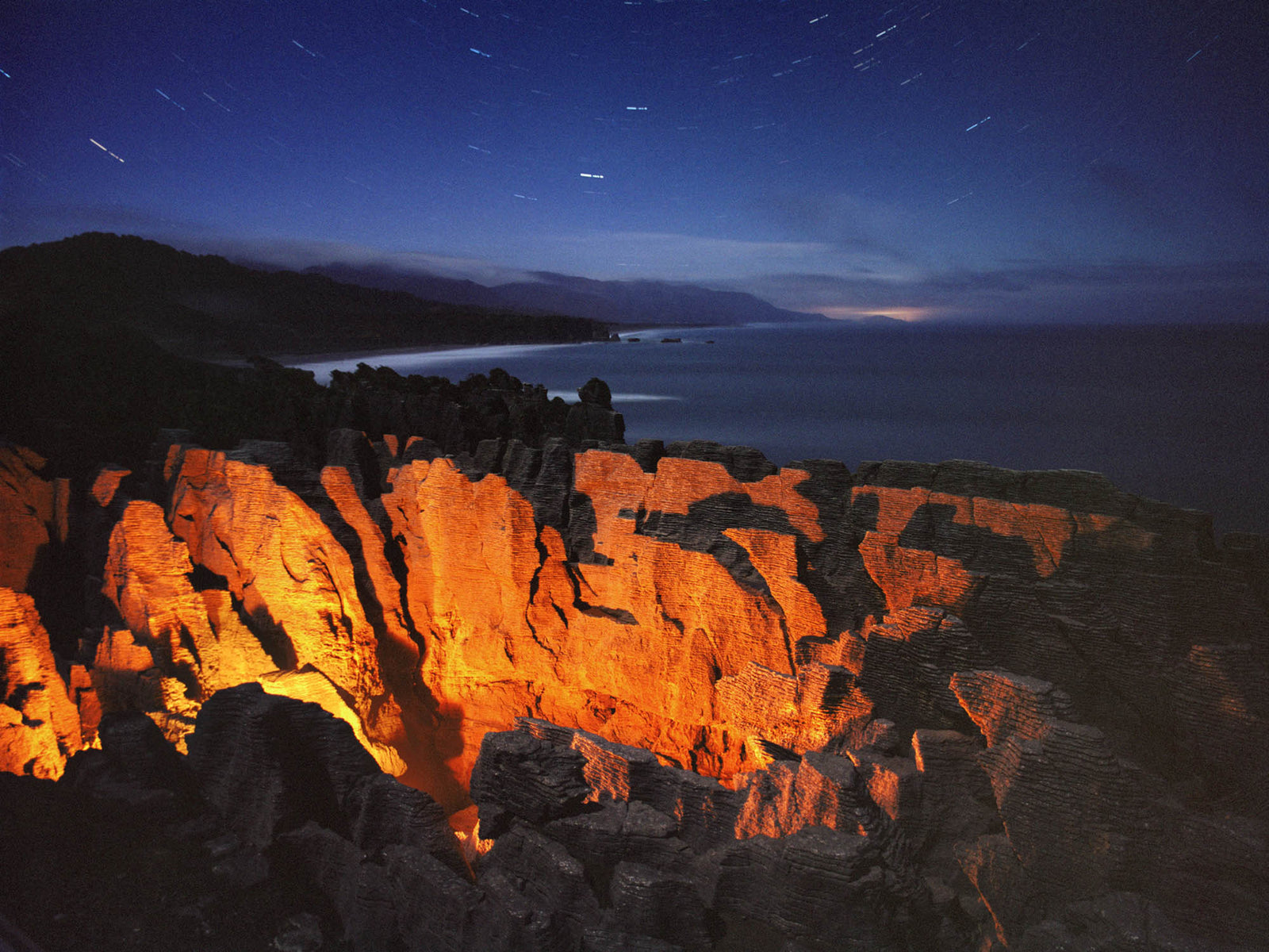 Photographie d’art d’André Wagner: Une lumière orange saisit les rochers accidentés du premier plan — Pancake rocks, Neuseeland.