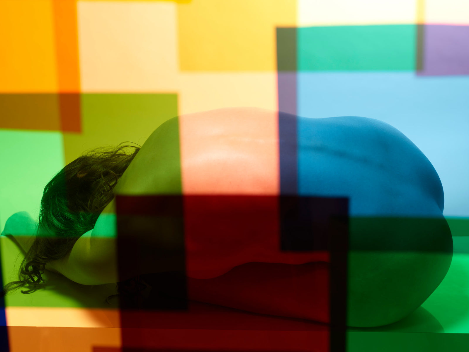 Photographie d’art d’André Wagner: Un corps nu replié sur lui-même est allongé horizontalement derrière des rectangles colorés — Paula I.