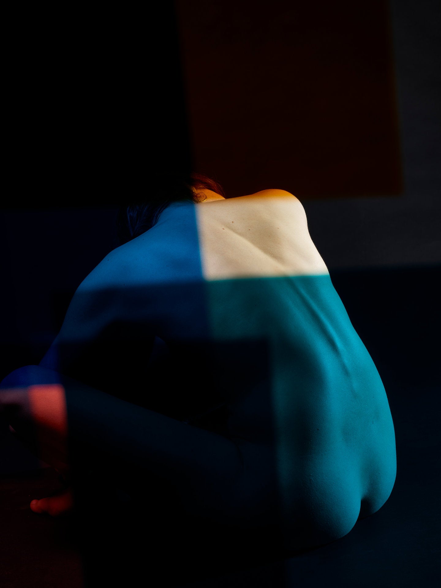 Photographie d’art d’André Wagner: Une figure assise, étroitement repliée, apparaît sur un fond presque noir — Paula XIII.