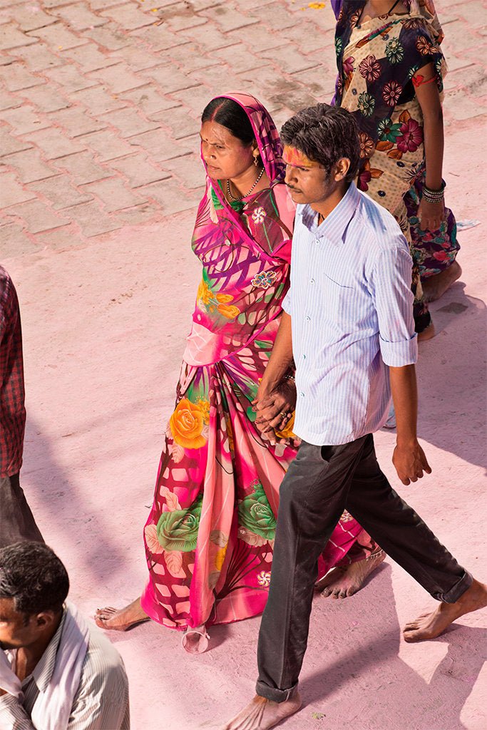Photographie d’art d’André Wagner: Une femme vêtue d’un habit rouge et vert aux motifs affirmés marche à côté d’un homme en chemise claire et pantalon sombre — Pilgrim on Purple Dust 13, Indien.