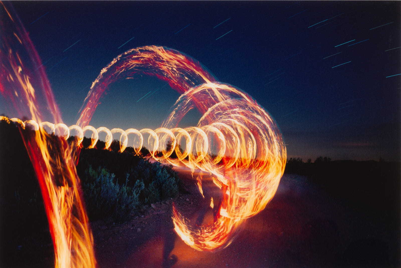 Photographie d’art d’André Wagner: Des trajectoires de lumière dorée et rouge forment de grandes boucles imbriquées devant un ciel nocturne sombre — Round the corner, Spanien.