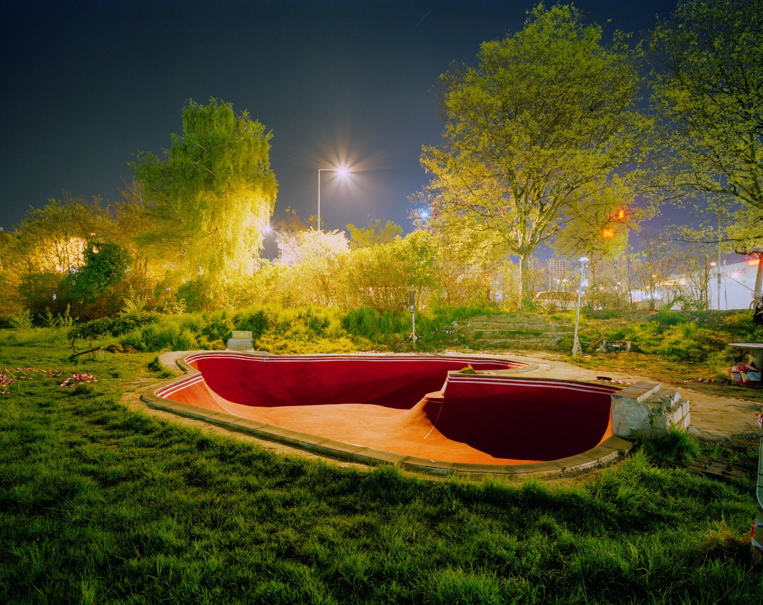 Photographie d’art d’André Wagner: Un skatepark rouge aux lignes courbes repose comme une vasque ouverte dans une surface verte — Skate Park, Schweiz.