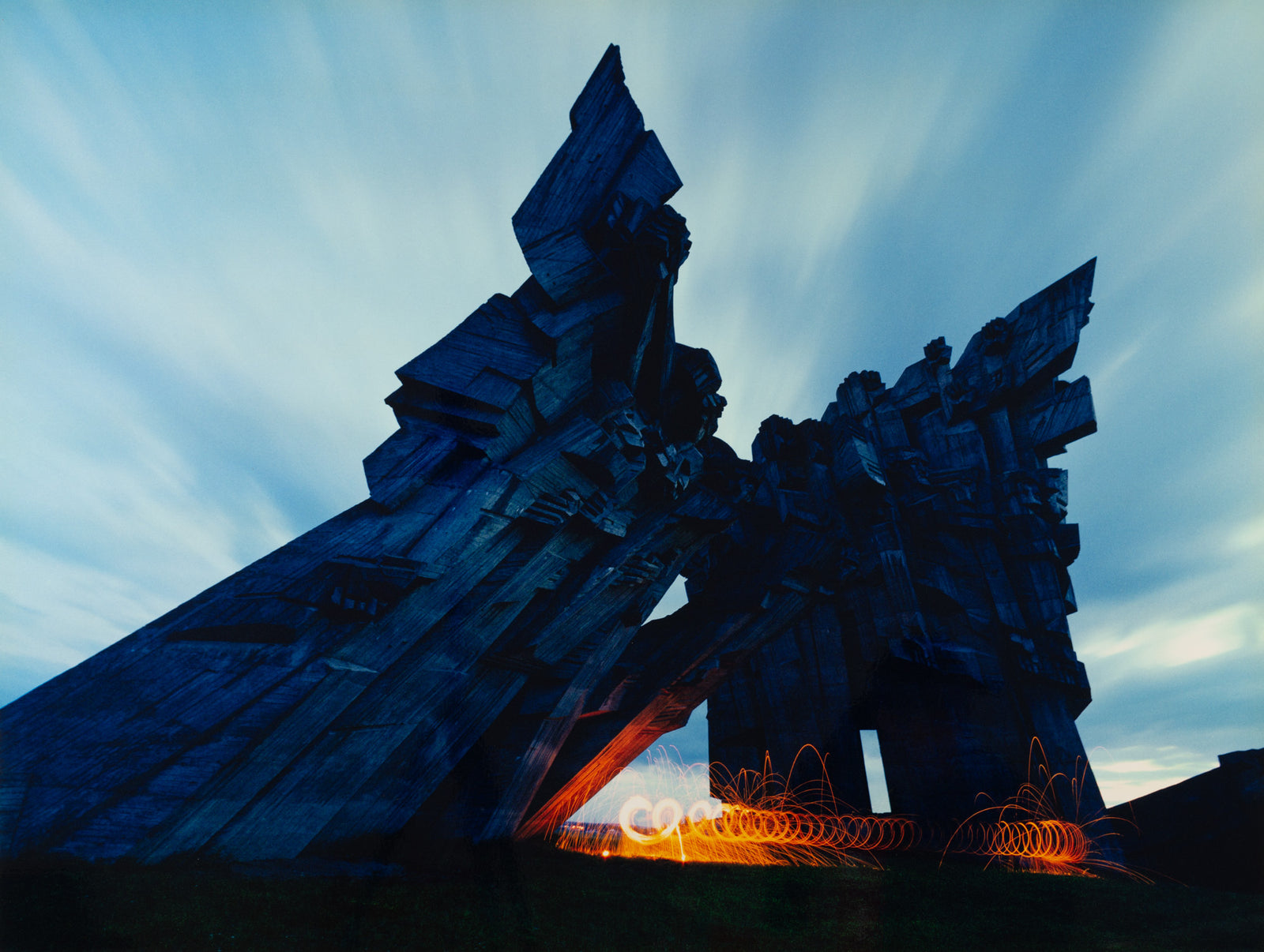Photographie d’art d’André Wagner: Des formes architecturales sombres aux arêtes vives s’élèvent dans plusieurs directions obliques devant un ciel clair strié — Softice on fire, Litauen.