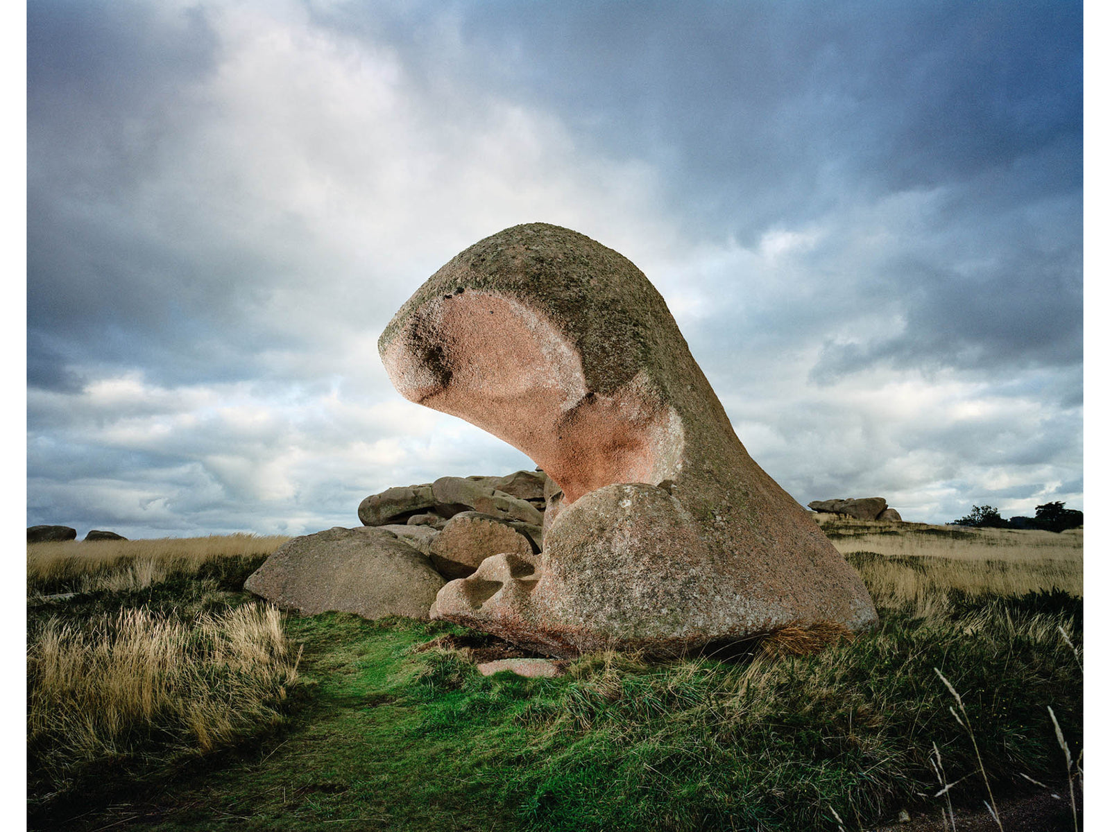 Photographie d’art d’André Wagner: Une grande pierre se dresse dans un paysage ouvert, sa partie supérieure courbée vers l’avant — Story of wind, Frankreich.