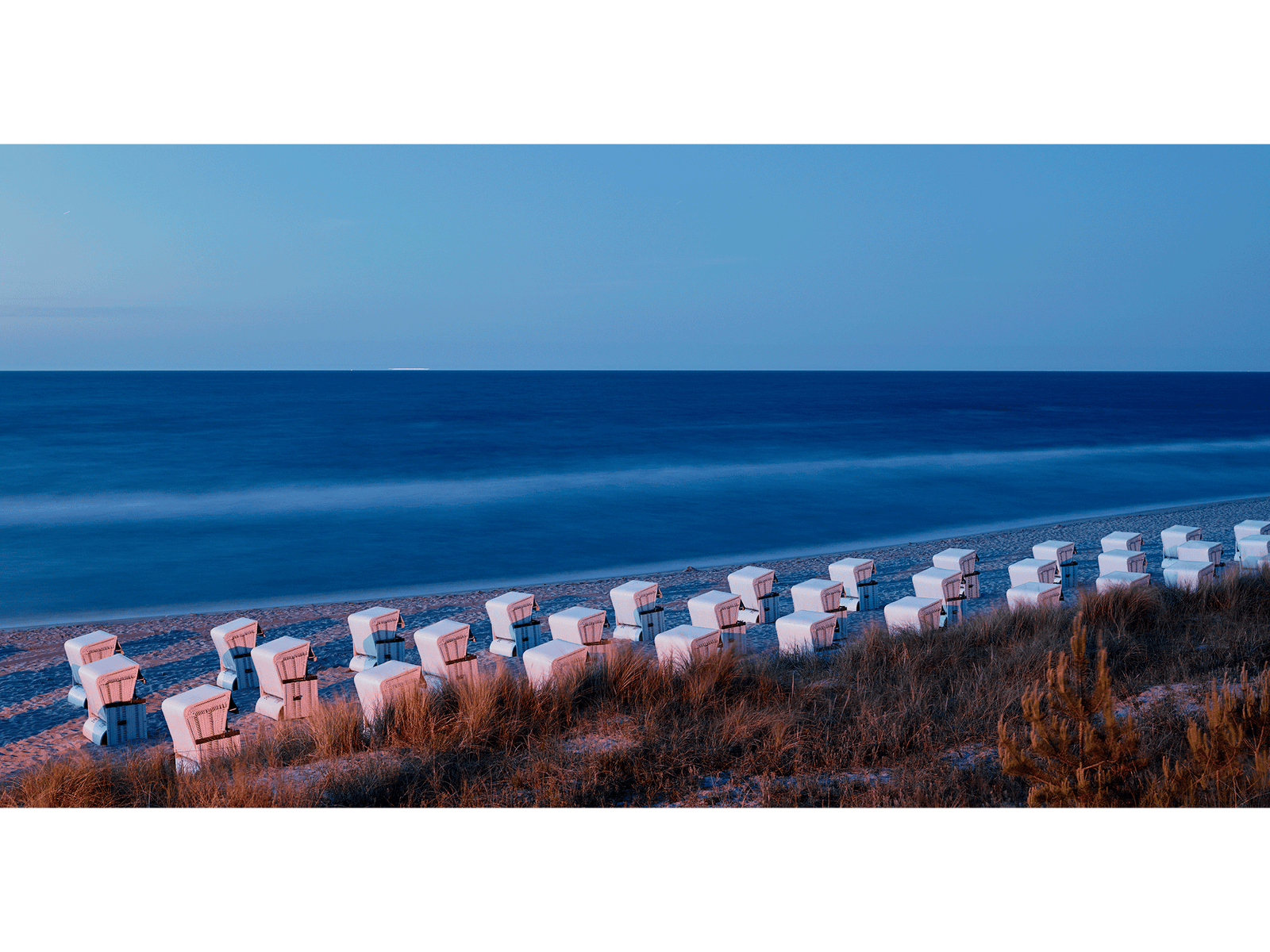 Photographie d’art d’André Wagner: Une longue rangée de fauteuils de plage à capote clairs suit le rivage — Strandkörbe zinnowitz 2, Deutschland.