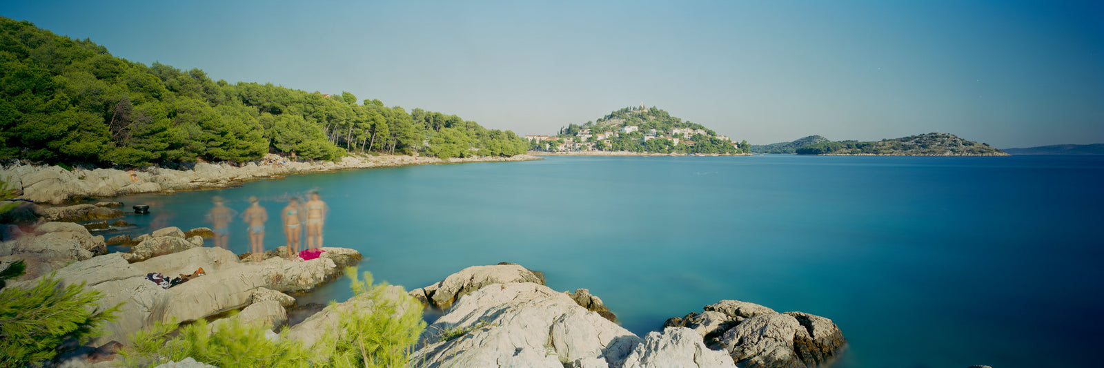 Photographie d’art d’André Wagner: Des rochers clairs avancent depuis la gauche dans une baie bleue calme — Talking.