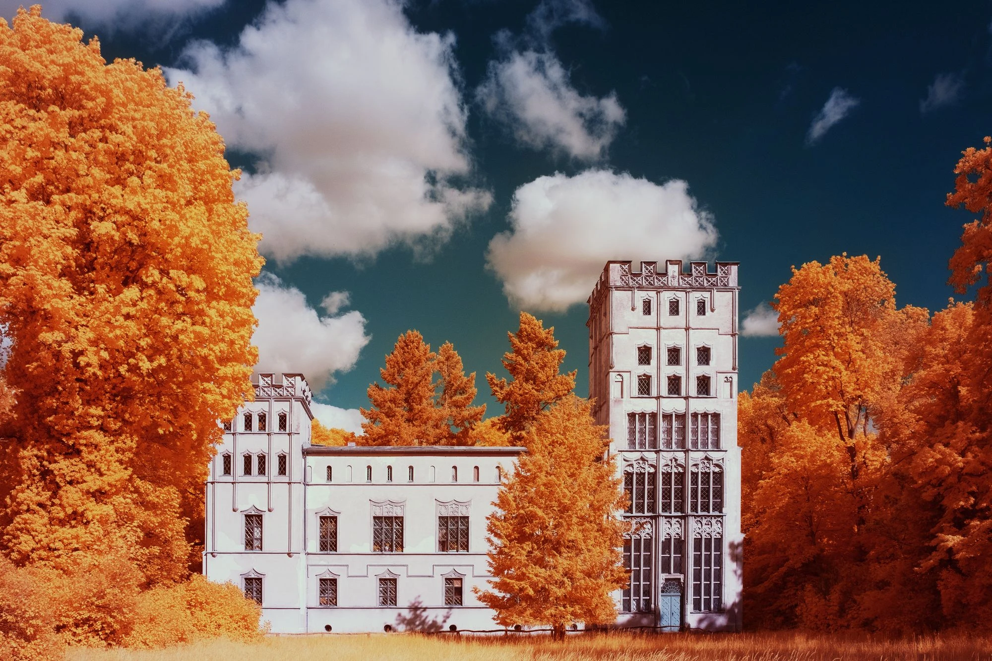 Photographie d’art infrarouge d’André Wagner: Entre des arbres orange doré se tient un bâtiment clair aux tours de hauteurs différentes — The Silent Pavilion.