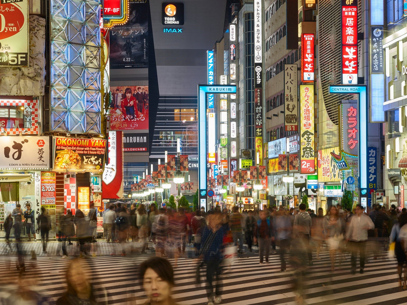 Fine art photography by André Wagner: Broad white road stripes lead towards densely lit façades — Tokyo Shinjuku 6.