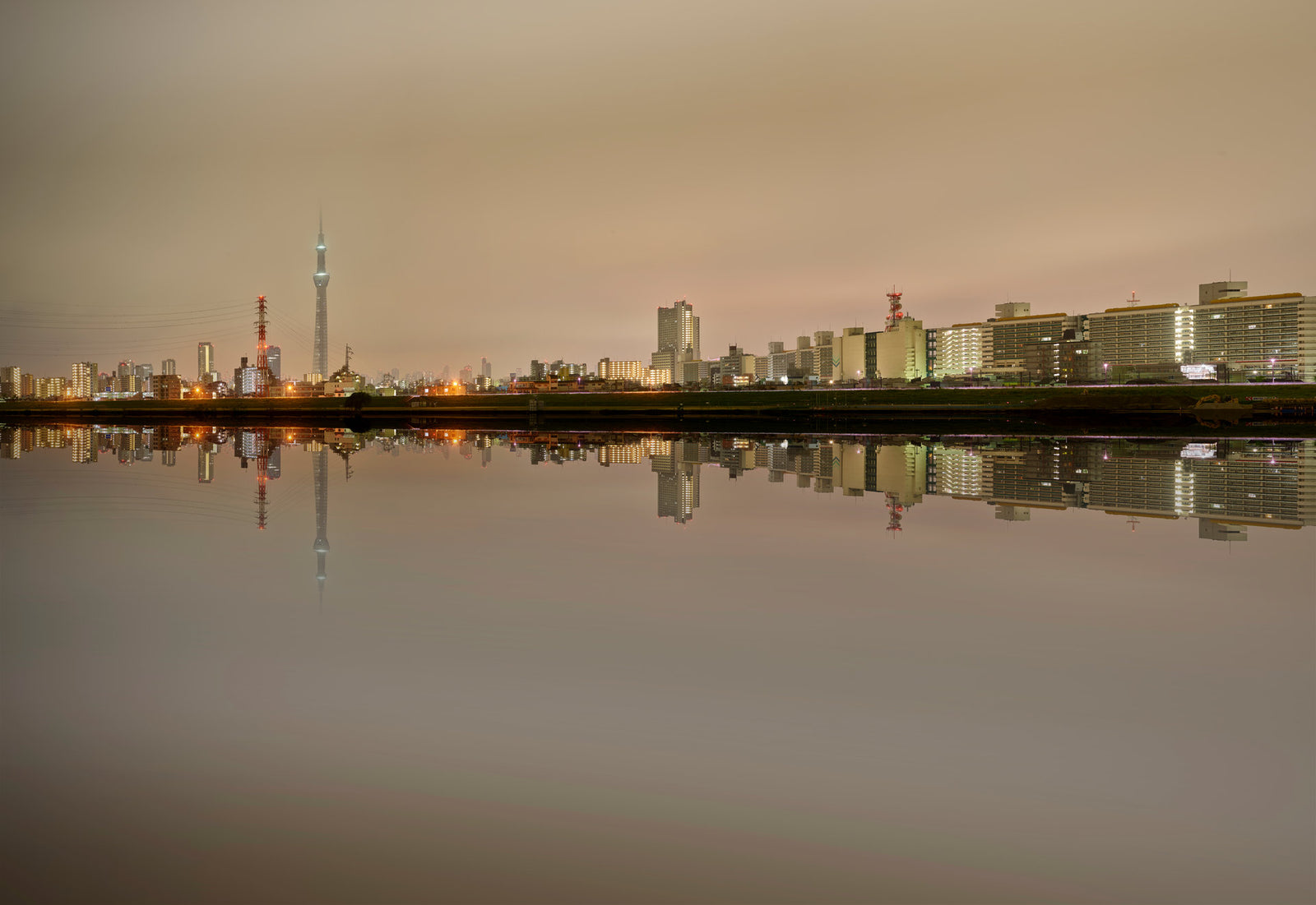 Photographie d’art d’André Wagner: Une longue silhouette urbaine s’étend au-dessus d’une eau presque lisse comme un miroir — Tokyo Skyline.