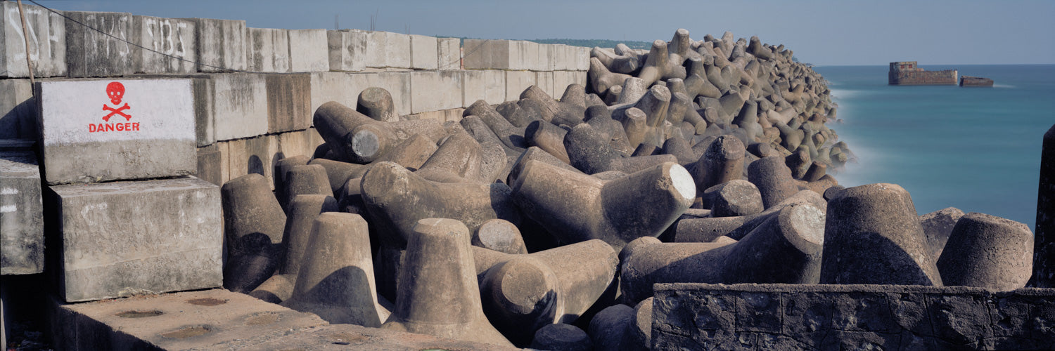 Photographie d’art d’André Wagner: Des formes de béton munies de plusieurs bras courts sont étroitement imbriquées contre un mur portuaire — Wave Breakers.