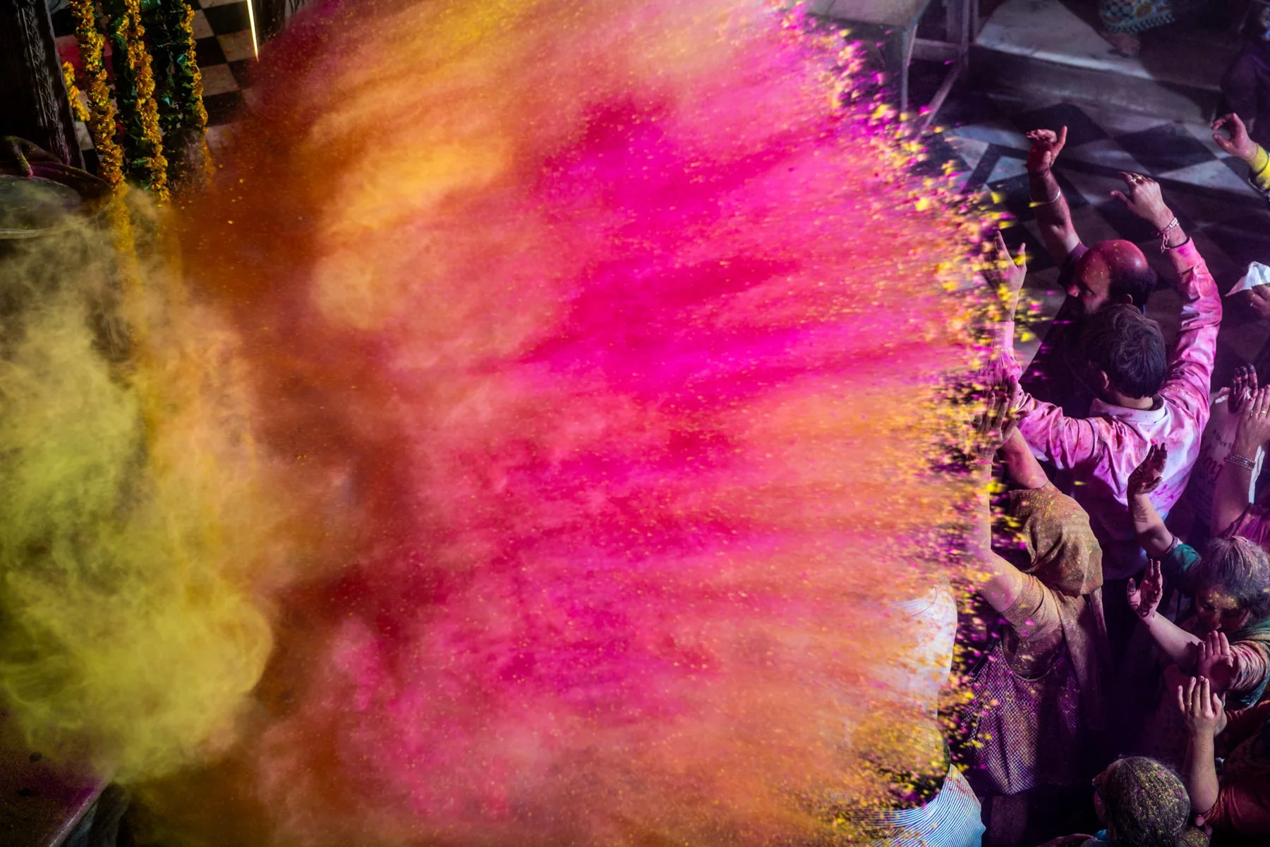 Wolke aus pinkfarbenem und gelbem Pulver &uuml;ber einer Menschenmenge beim Holi-Fest.