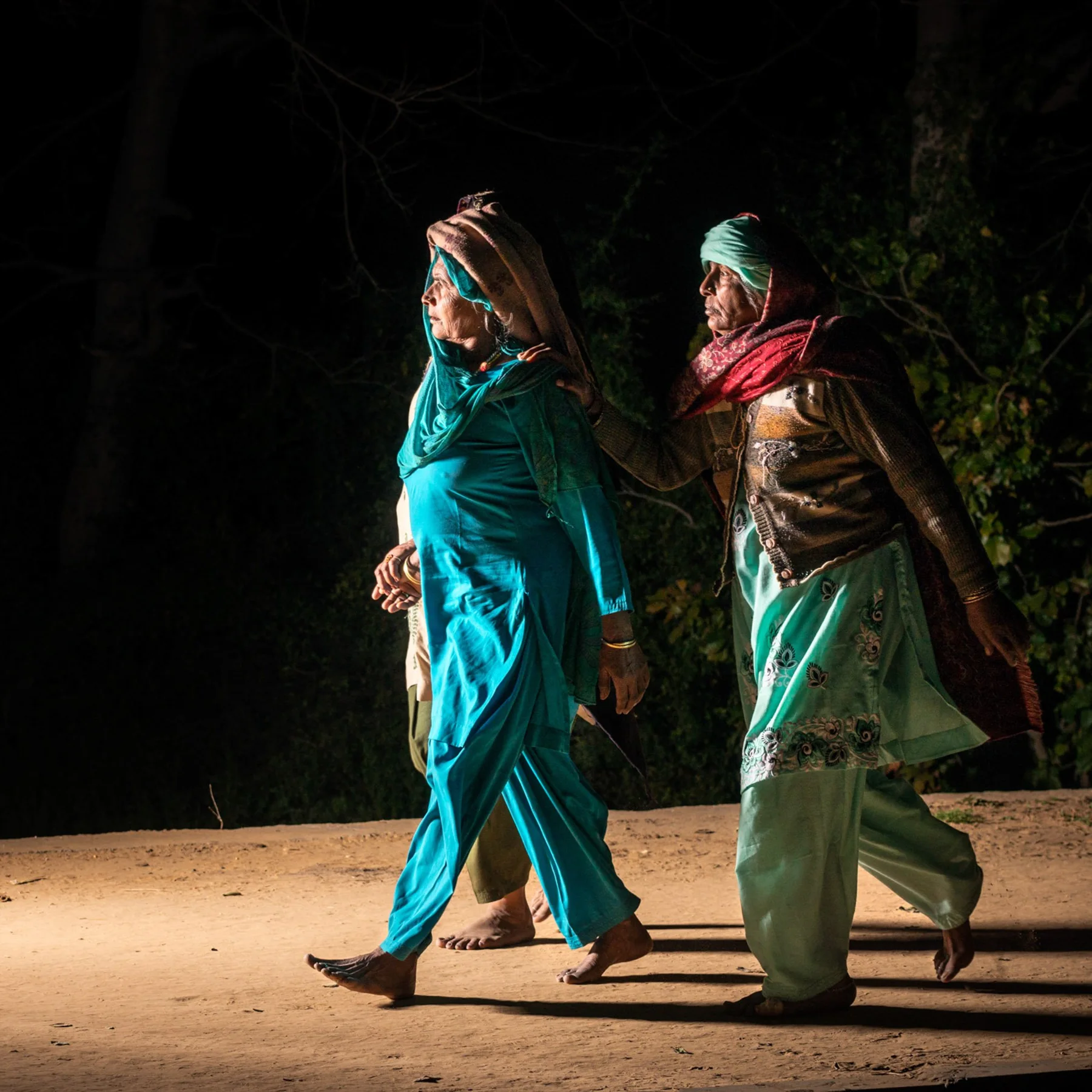 Zwei Frauen in t&uuml;rkisfarbenen und gr&uuml;nen Gew&auml;ndern auf einer Stra&szlig;e bei Nacht.