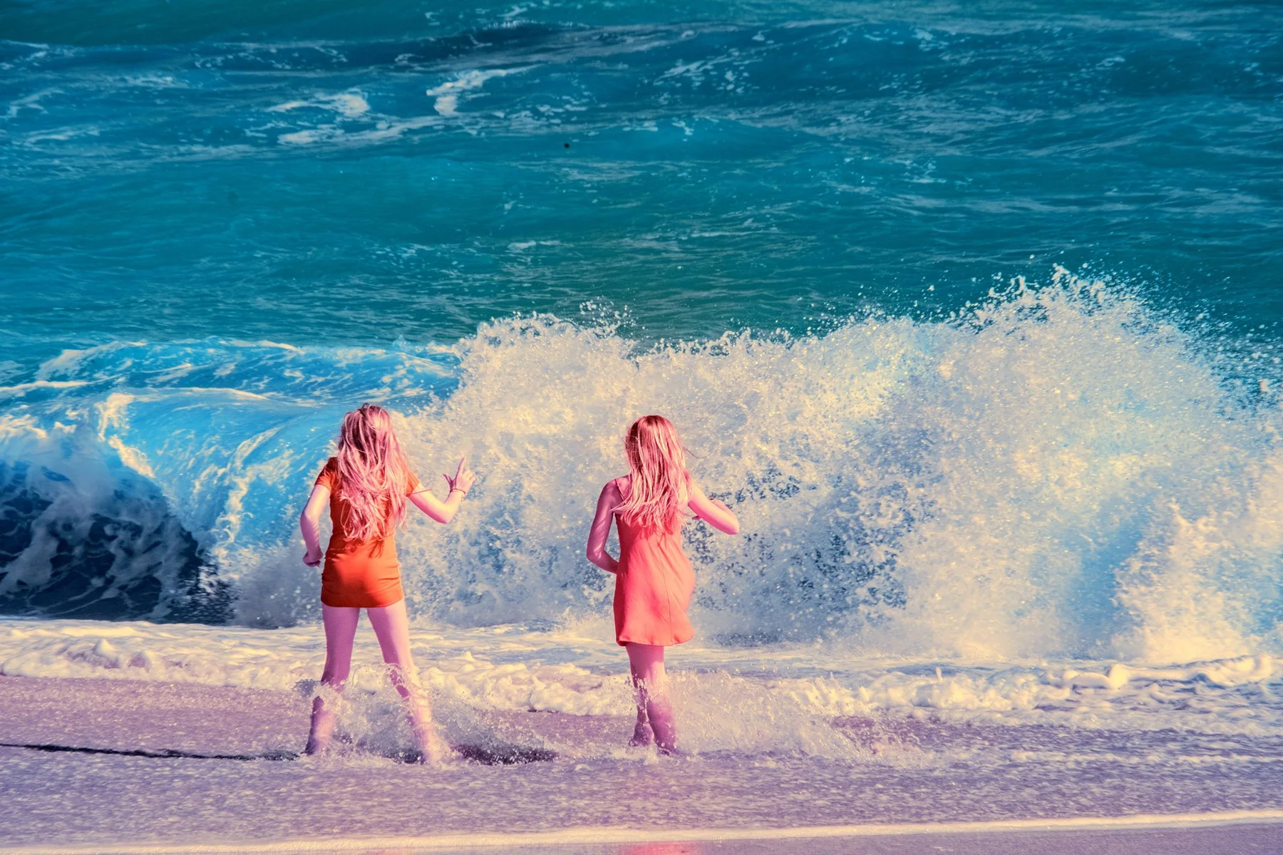 Deux personnes sur la plage devant une grande vague.