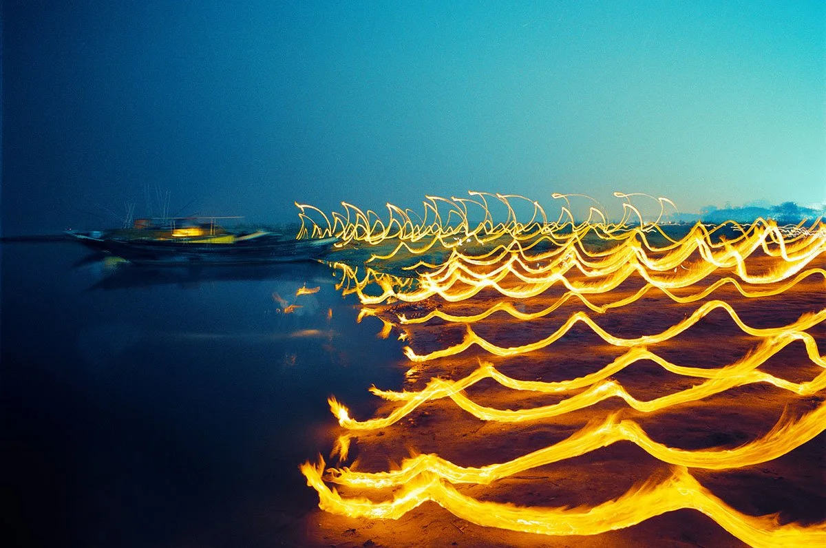 Wellenförmige goldene Lichtspuren über dunklem Wasser unter einem blauen Nachthimmel.