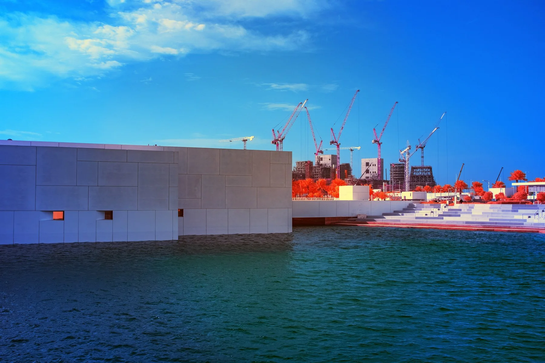 Wei&szlig;er Museumsbau am Wasser mit Baukr&auml;nen im Hintergrund.