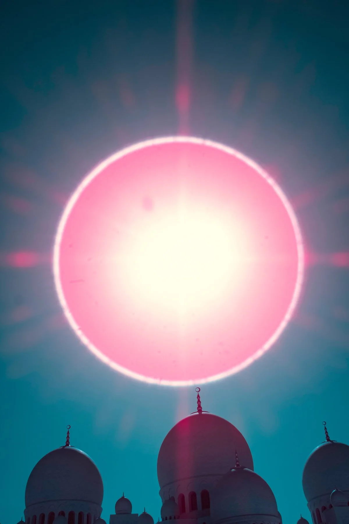 Pinkfarbener Lichtkreis &uuml;ber den Kuppeln einer Moschee.