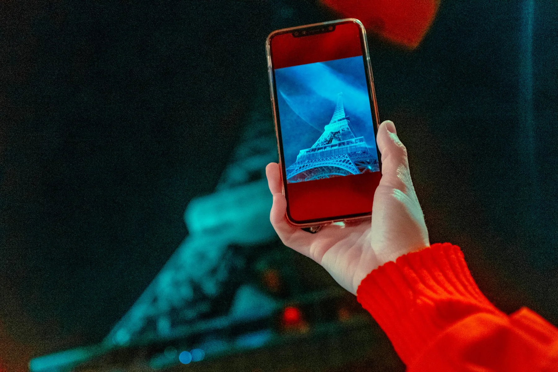 Ein Smartphone vor dem beleuchteten Eiffelturm.