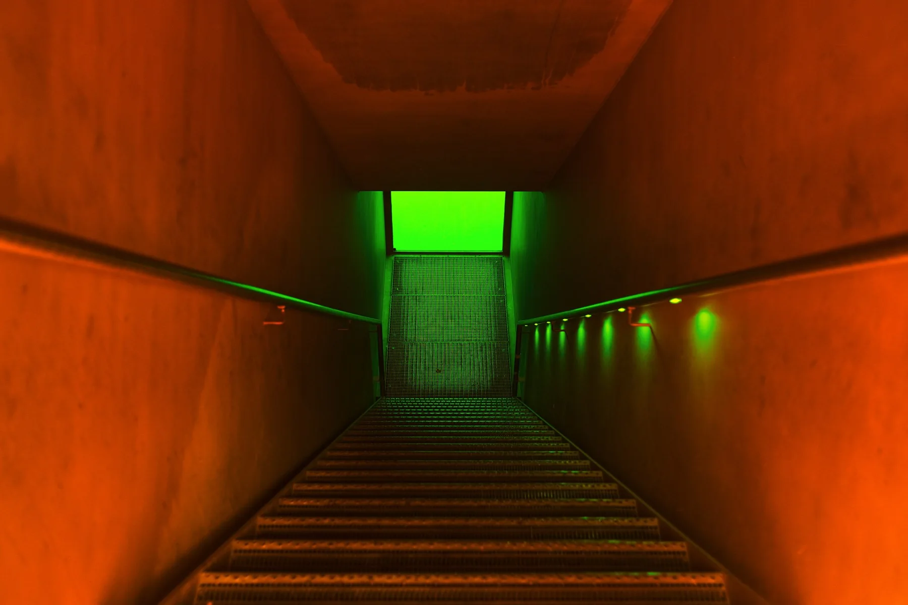 Treppe durch einen orangefarbenen Gang zu einer gr&uuml;n leuchtenden T&uuml;r.