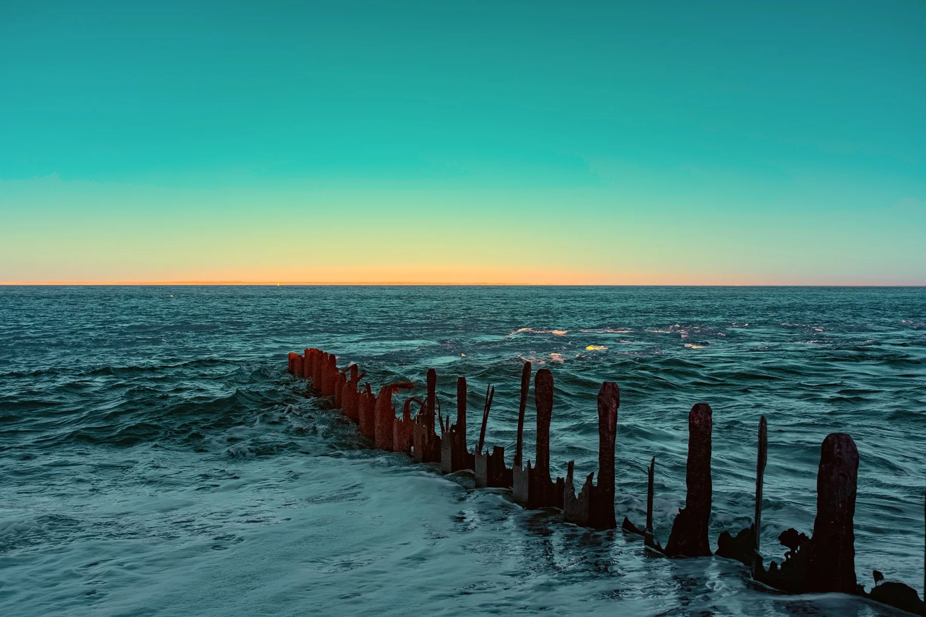 Reihe verwitterter Holzpf&auml;hle im Meer.