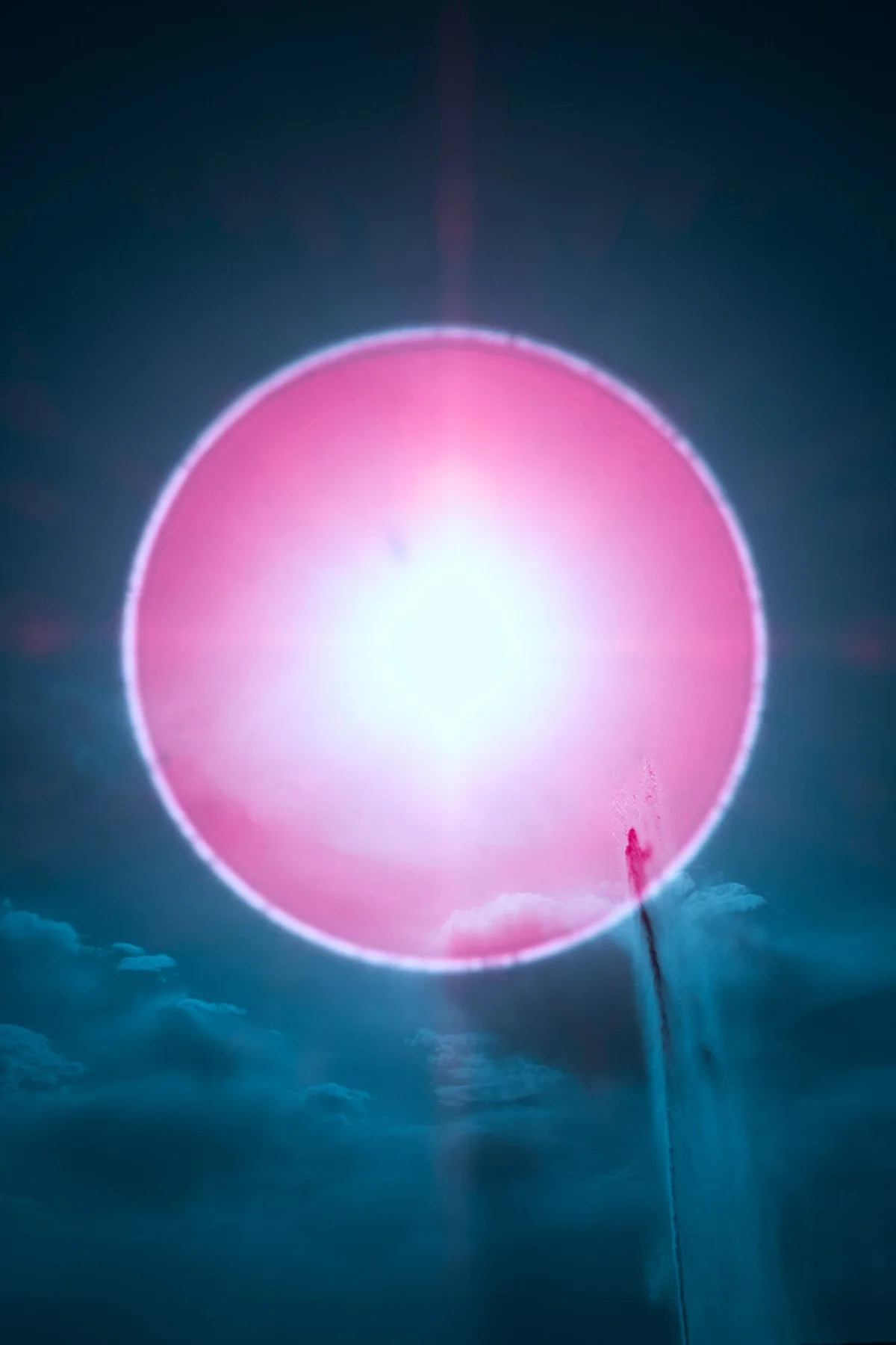 Pinkfarbener Lichtkreis vor blauem Himmel und Wolken.