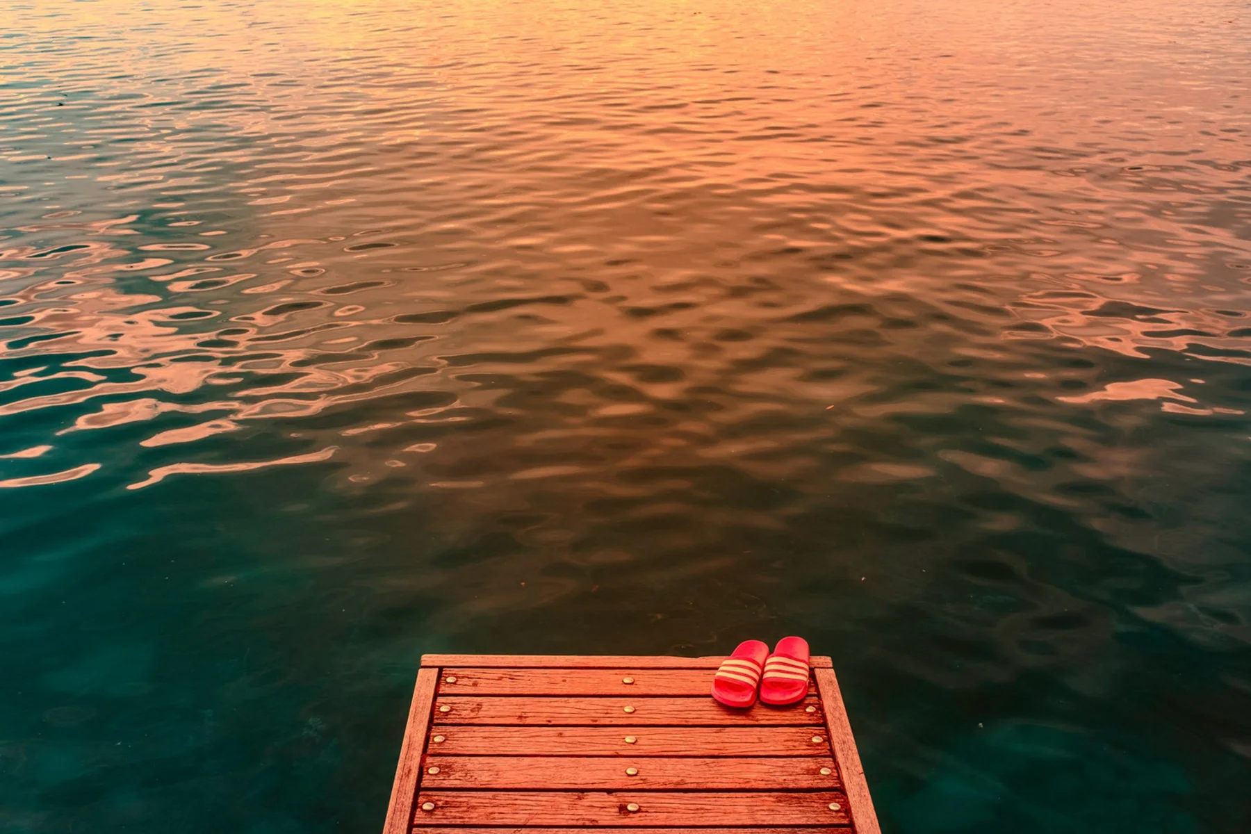 Rote Schuhe auf einem Holzsteg am Wasser.