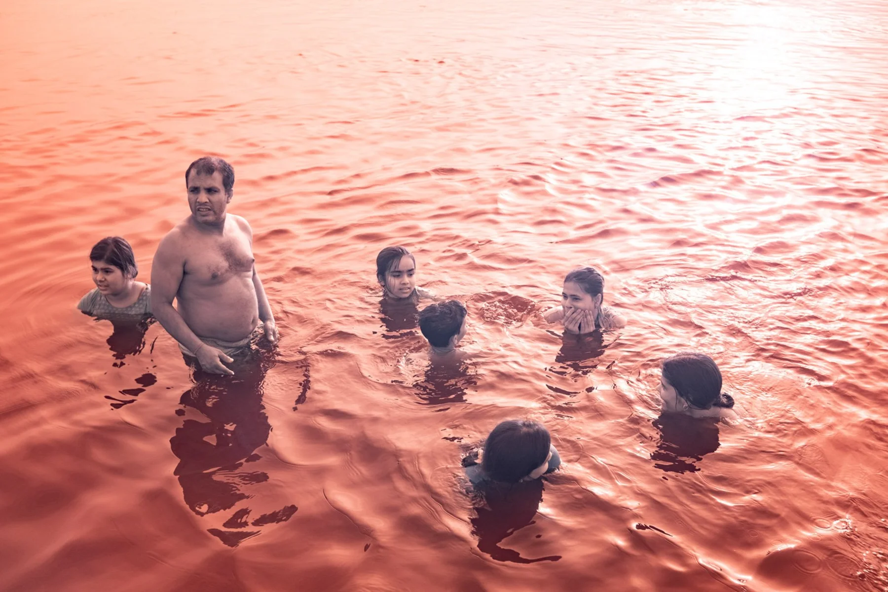 Mehrere Menschen stehen in orange gef&auml;rbtem Wasser.
